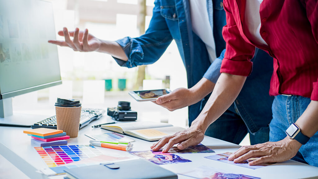 Dos personas trabajando sobre una mesa. Se ven gráficos y material para escribir, ordenadores. Se aprecia cómo están debatiendo sobre la estrategia publicitaria